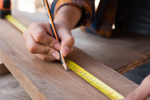 Person marking measurement with a pencil on a piece of wood