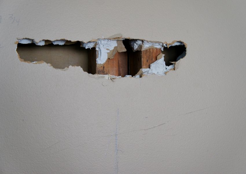 large hole in grey dry-wall exposing wood studs