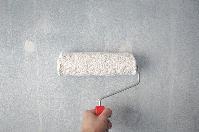 white paint roller being used on the faded white-grey wall