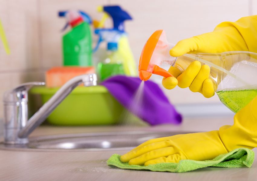 hands in yellow cleaning gloves holding a spray bottle with cleaning solution in it